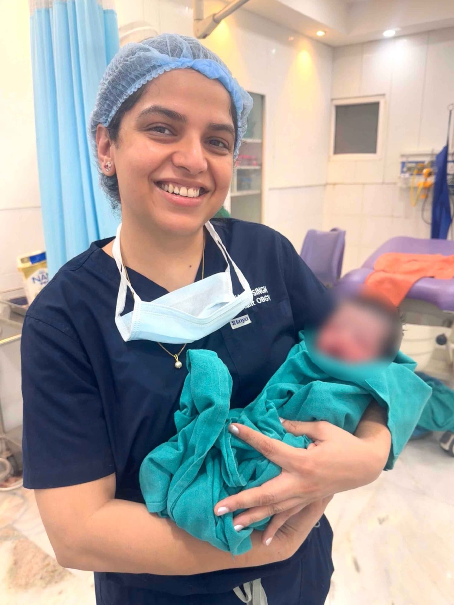 Dr. Shachi Singh in scrubs and a surgical cap holding a newborn baby moments after delivery