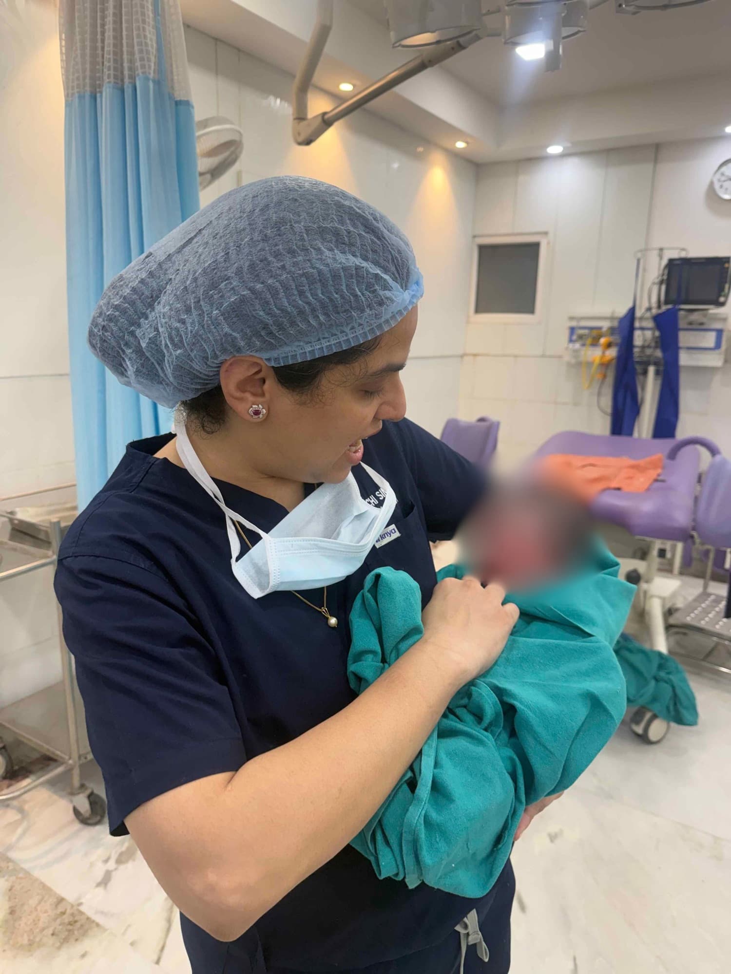 Dr. Shachi Singh cradling a newborn swaddled in teal after a delivery at Prakash Hospital