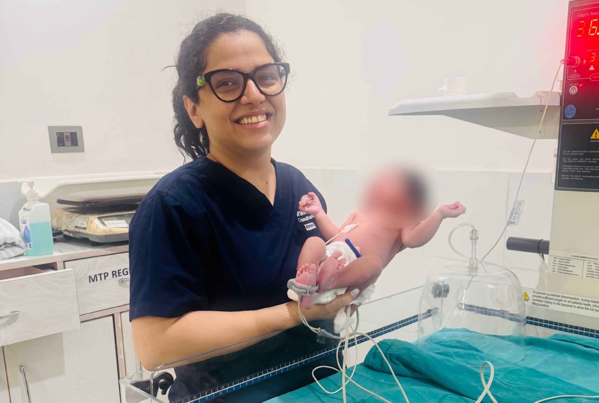 Dr. Shachi Singh holding a newborn baby beside the infant warmer in the newborn care unit