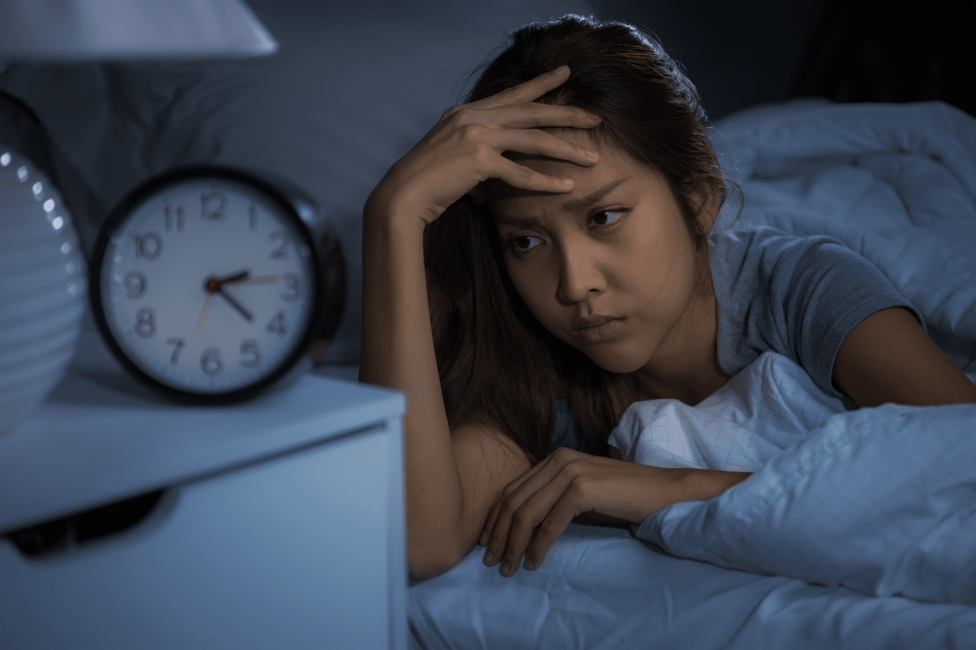A woman lying awake at night beside an alarm clock, looking stressed, illustrates the lack of proper sleep as a major cause of hormonal imbalance.
