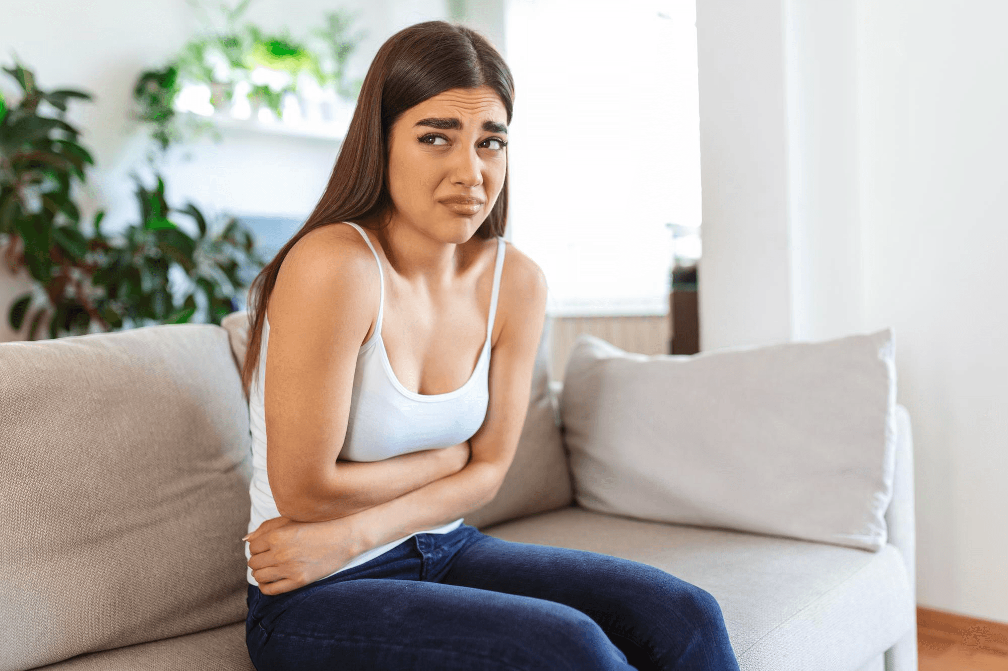 Woman sitting on the sofa, clutching her stomach due to severe PCOS cramping with a pained expression.