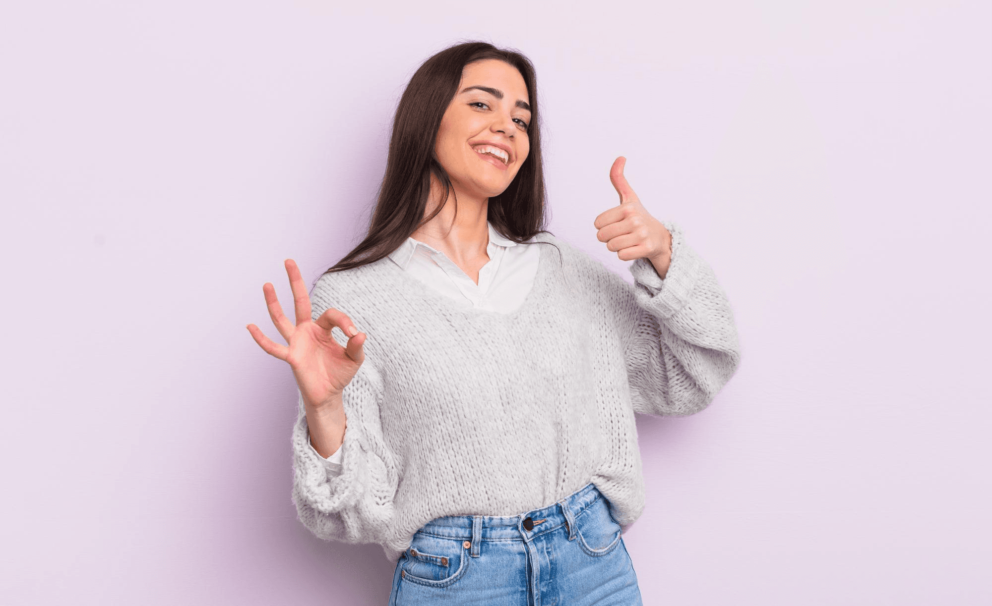 A young woman, happy, amazed, satisfied, and surprised, showing an OK and thumbs-up gesture, smiling.