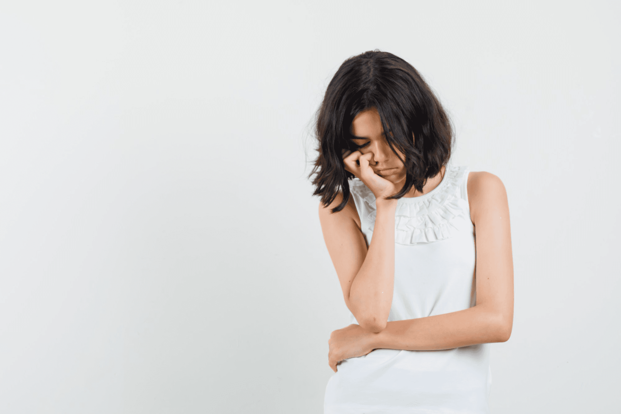 Girl in a white background, in a thinking pose, looking sad and distressed.