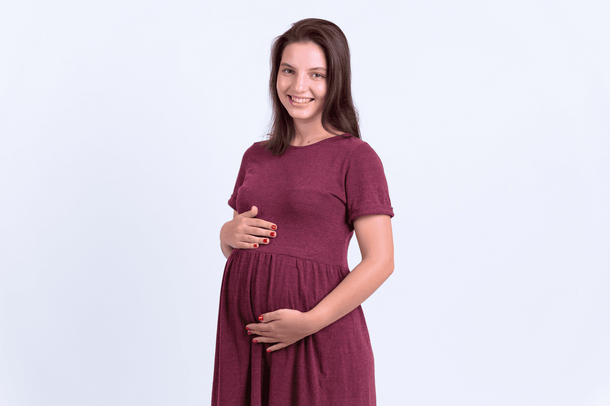 Woman in her 8th month of pregnancy, holding her belly happily against a white background.