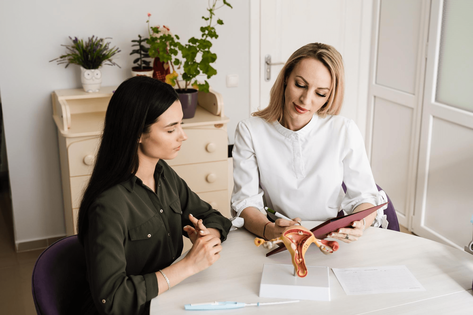 Woman talking with a gynecologist about vaginal hygiene and reproductive health while the doctor uses a uterus model during their appointment.