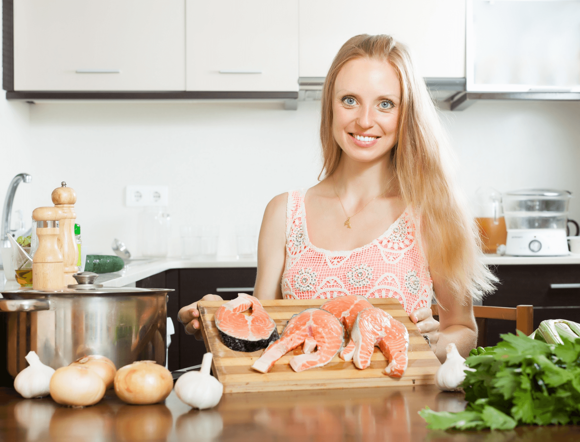 Woman holding fresh salmon slices in her kitchen, showing off omega-3-rich fish that help balance hormones and boost fertility.