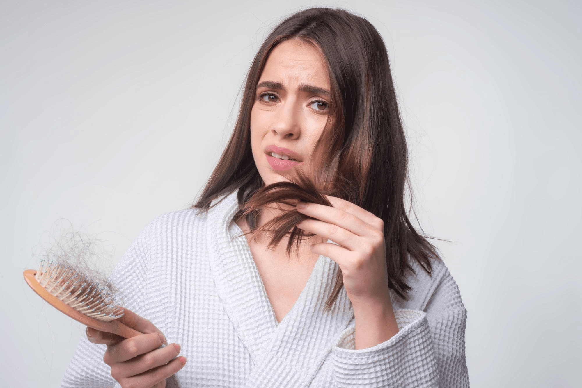 Woman examining strands of hair and hairbrush showing hair loss and reflecting possible nutritional deficit in anemia during pregnancy.