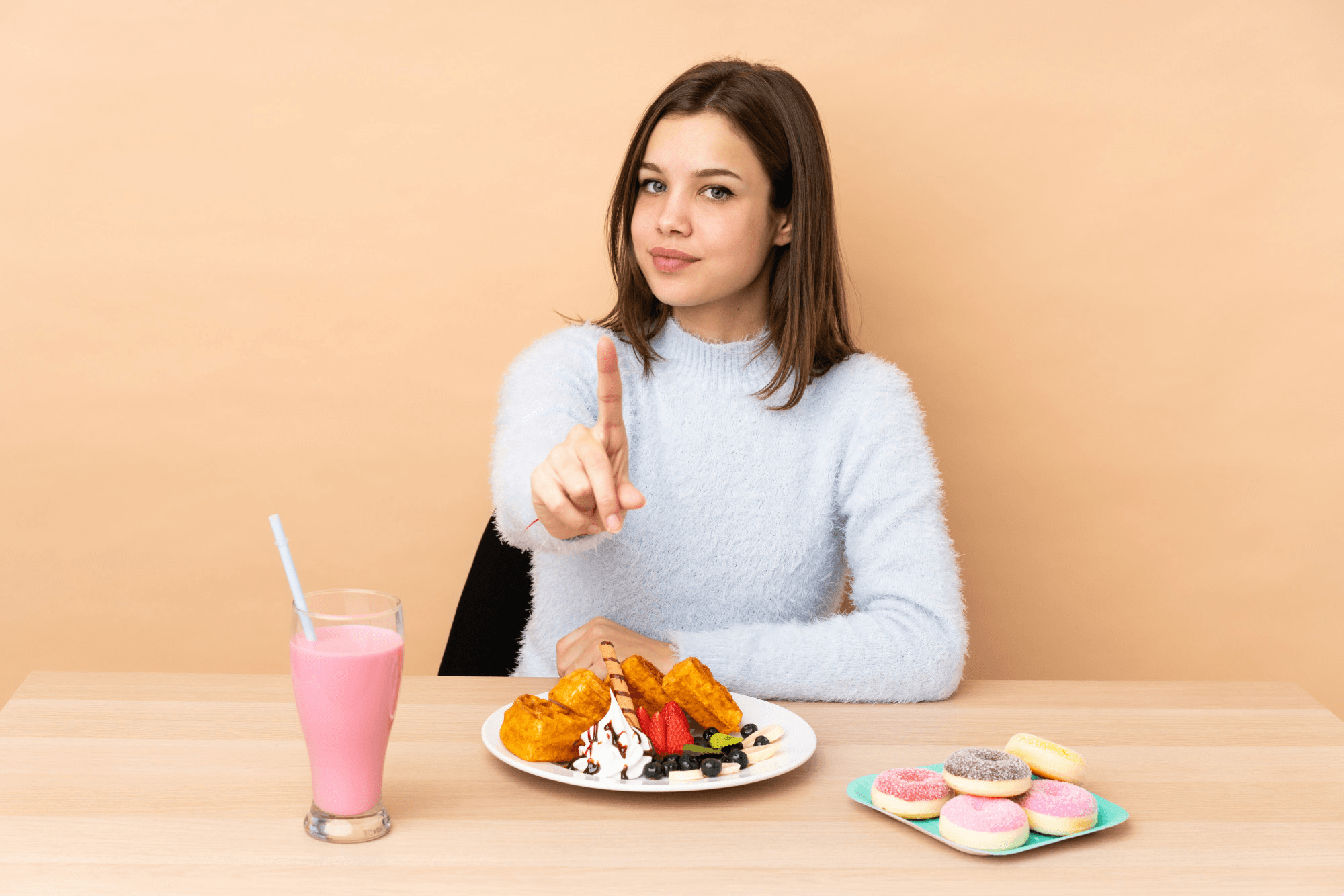 A woman rejects unhealthy sweets while eating a smoothie, emphasizing mindful eating for a healthy lifestyle, indoors