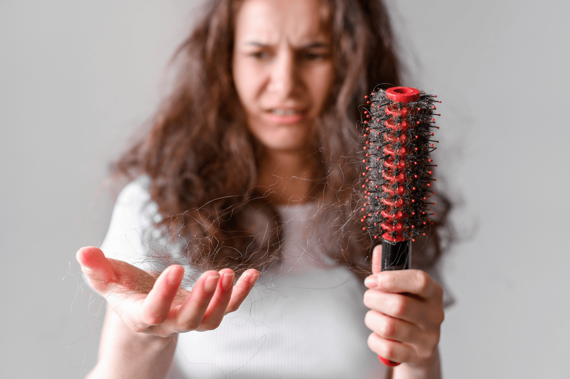 Concerned woman holding a hair brush full of falling hair, indicating thinning hair among perimenopause symptoms.
