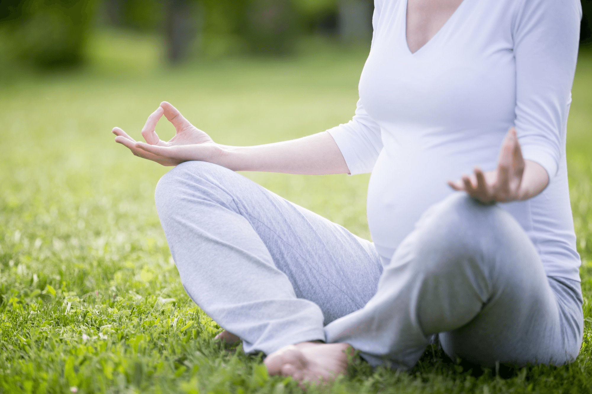 Pregnant woman in a posture of meditation while outdoors in nature, with her legs crossed while in the prayer posture, so she can be peaceful and remain mentally calm.