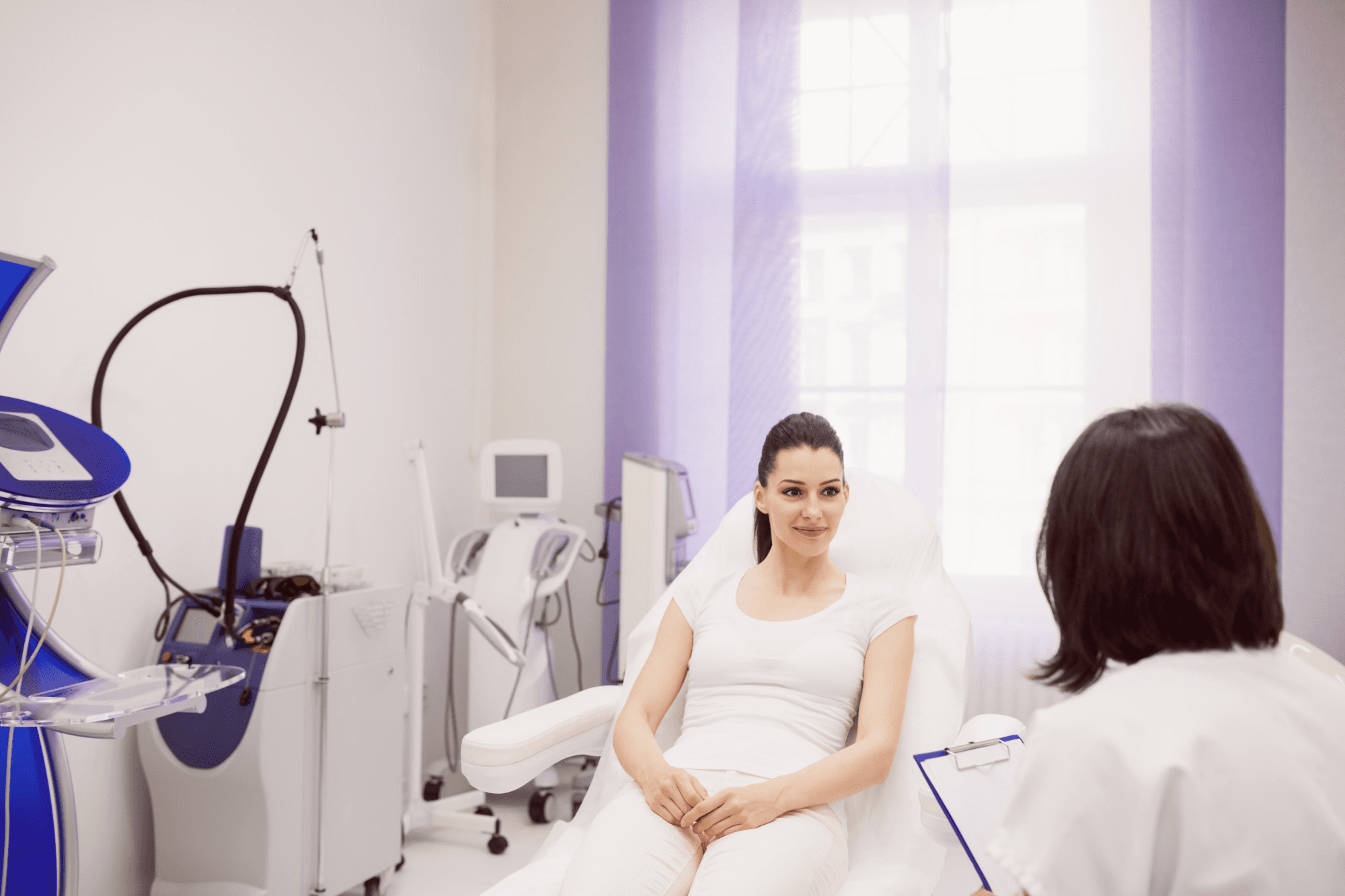 It shows a woman being addressed by a professional about the vaginal cosmetic procedure while being made to feel comfortable with all the necessary instruments displayed in the background.