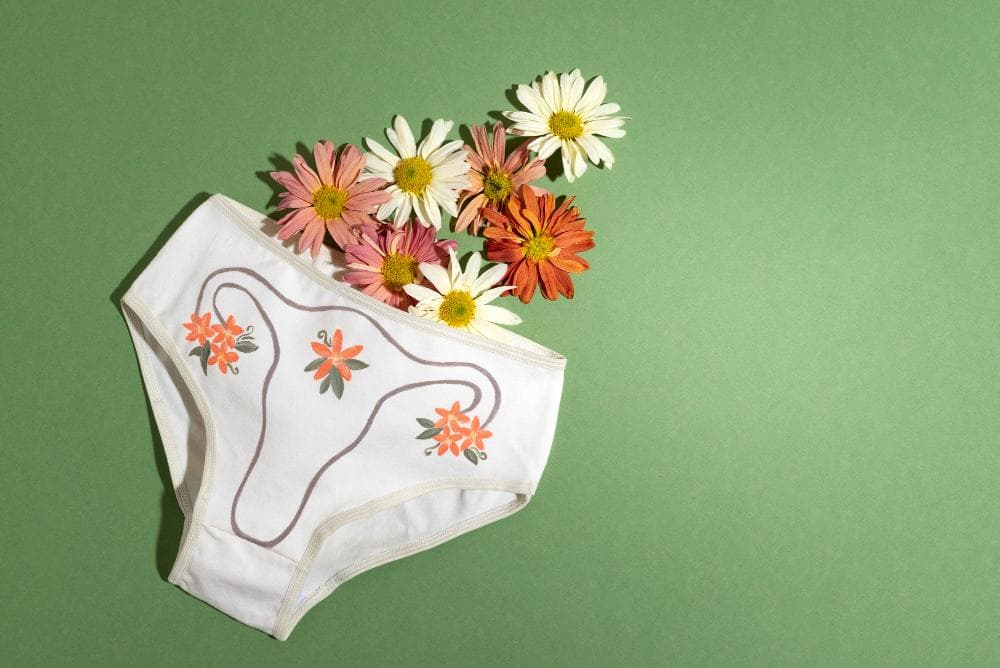 White cotton underwear with floral print and colorful flowers arranged inside as a sign for feminine hygiene and health, and feminine reproductive health on a green background.