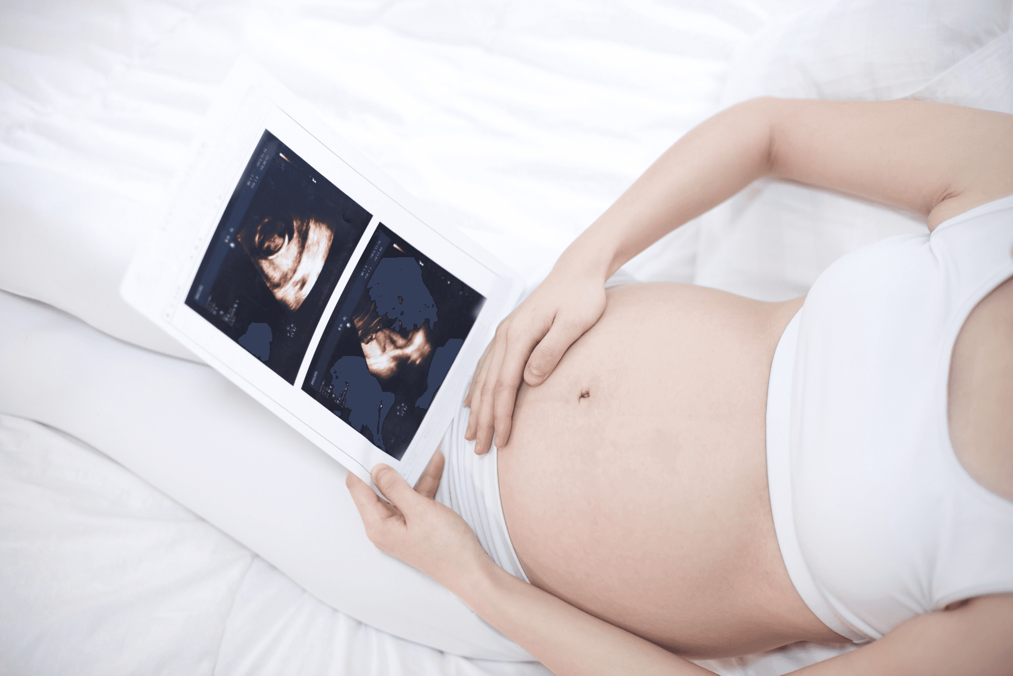 Pregnant woman holding ultrasound scans over baby bump while lying down.