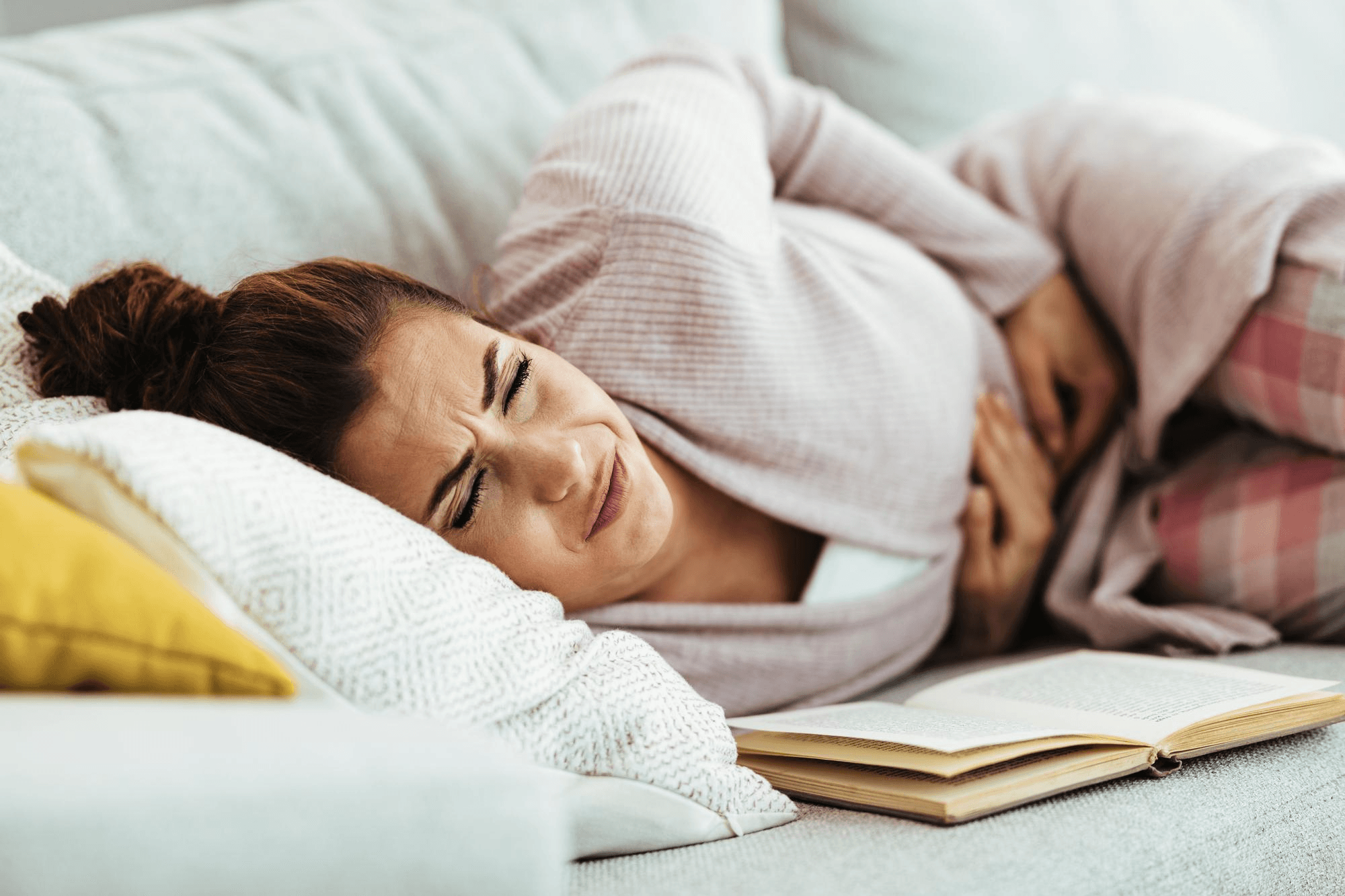 Female patient lying on the couch with her hand on her abdomen, while clearly in pain, the reason may be blocked fallopian tubes